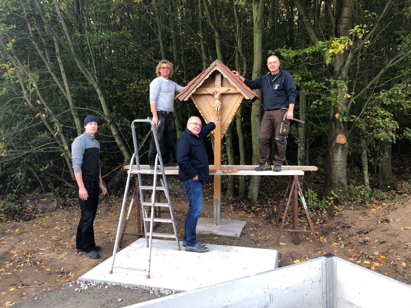 Von links: Dariusz Balcerski mit seinem Chef, Dachdeckermeister Andreas Bonnet, Schreinermeister Michael Erbacher und Bürgermeister Reinhold Hehmann vor dem Wegkreuz in Radheim - zu erreichen über die Große Hohl zum ehemaligen „Radheimer Turm“ am Waldrand